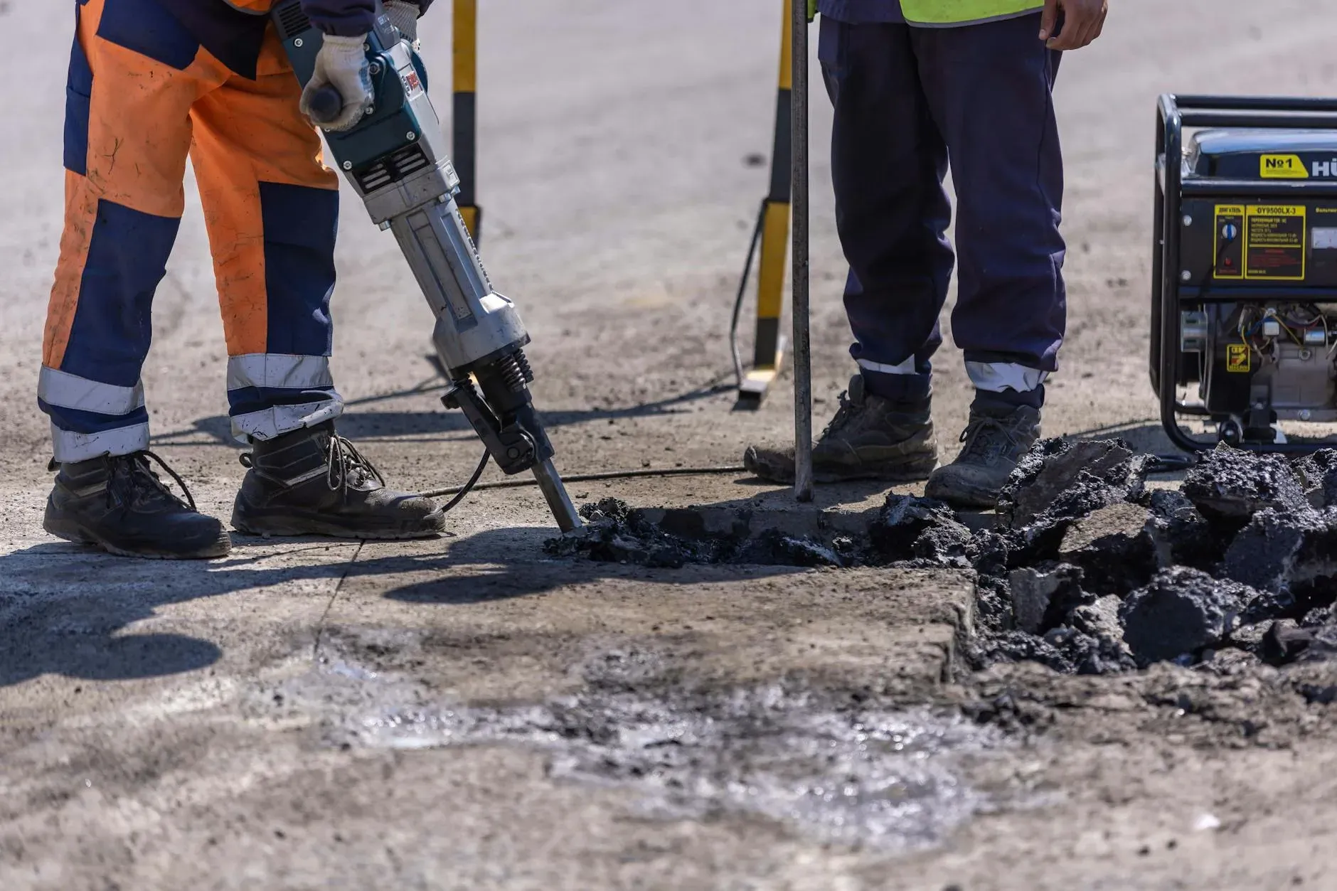 Durante i lavori stradali, gli operai edili rompono l'asfalto con un martello pneumatico.