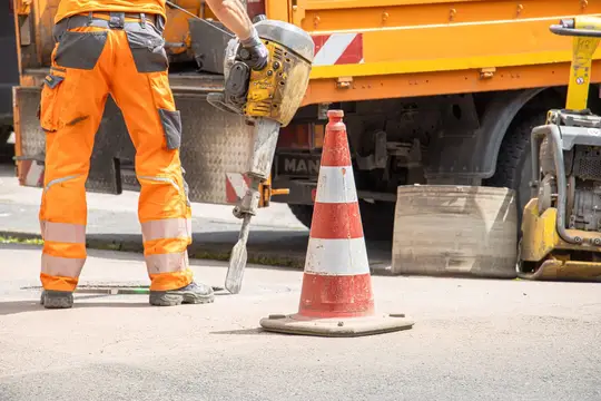 Thomas Fuhrmann Operaio edile con martello pneumatico accanto a un cono stradale su una strada cittadina